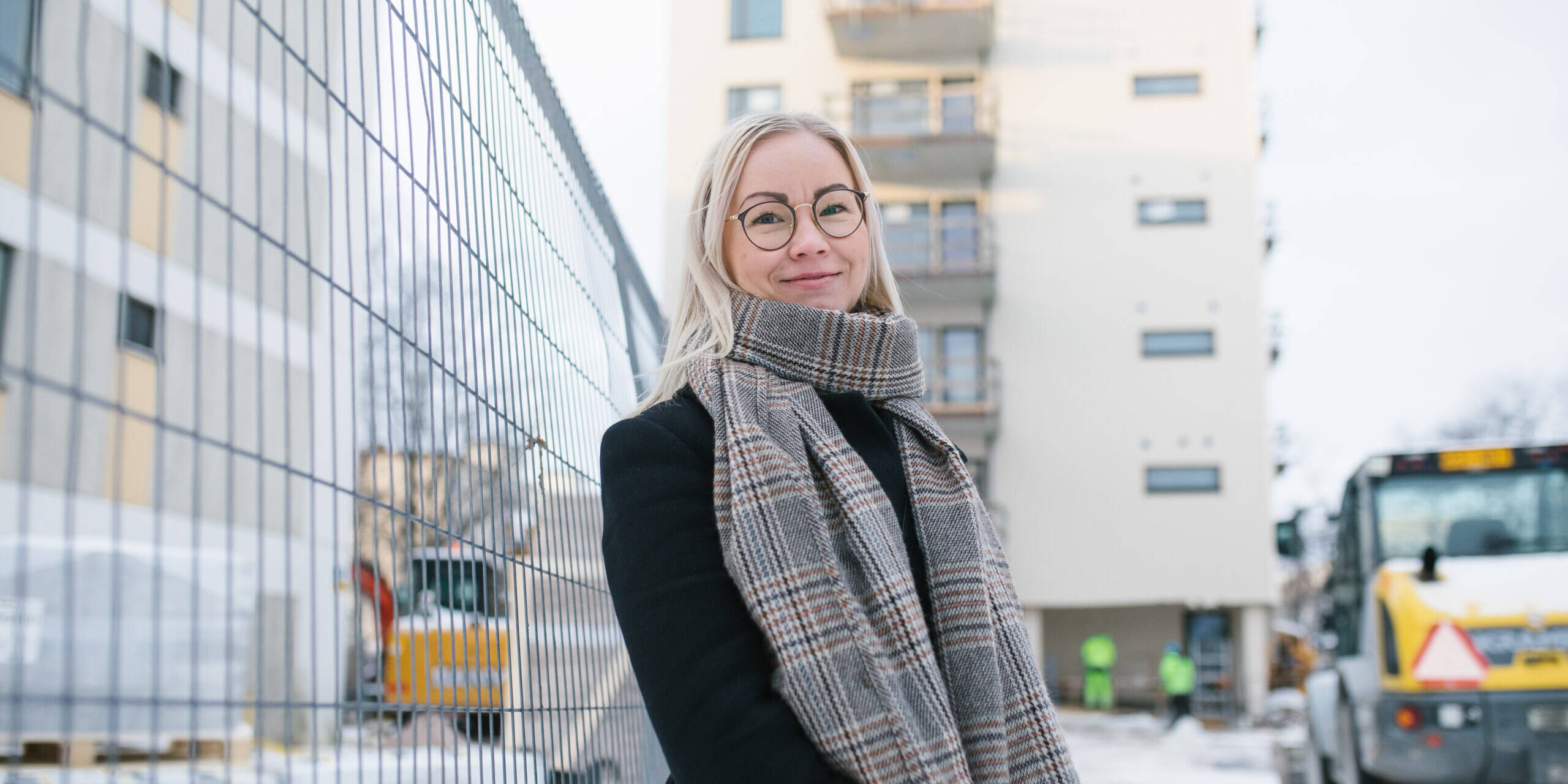 A person is standing on a construction site, with a house and a tractor in the background.