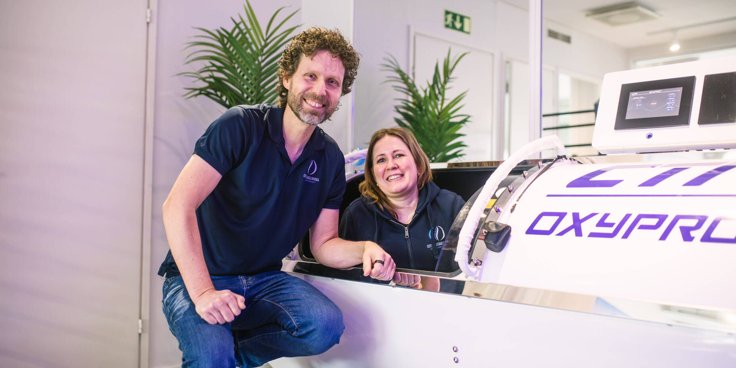 Mies ja nainen kapselin luona poseeraamassa kameralle.