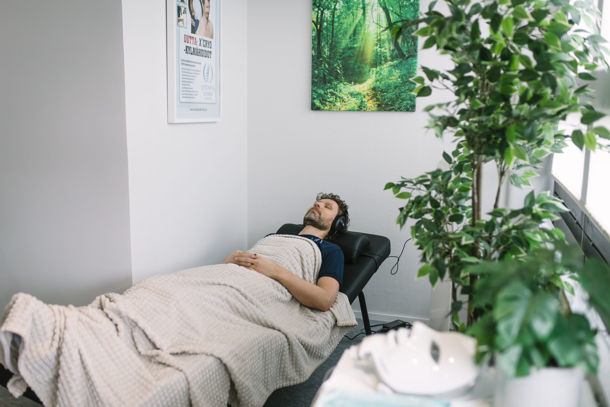 Mies makaa viltin alla kuulokkeet korvilla vieressään viherkasveja.