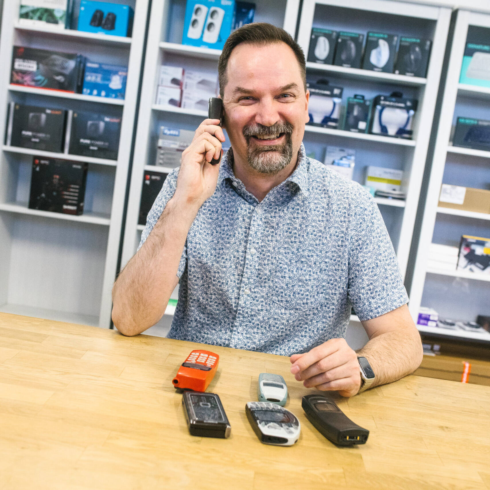 Henkilö puhumassa vanhaan puhelimeen. Edessä vanhoja puhelimia.