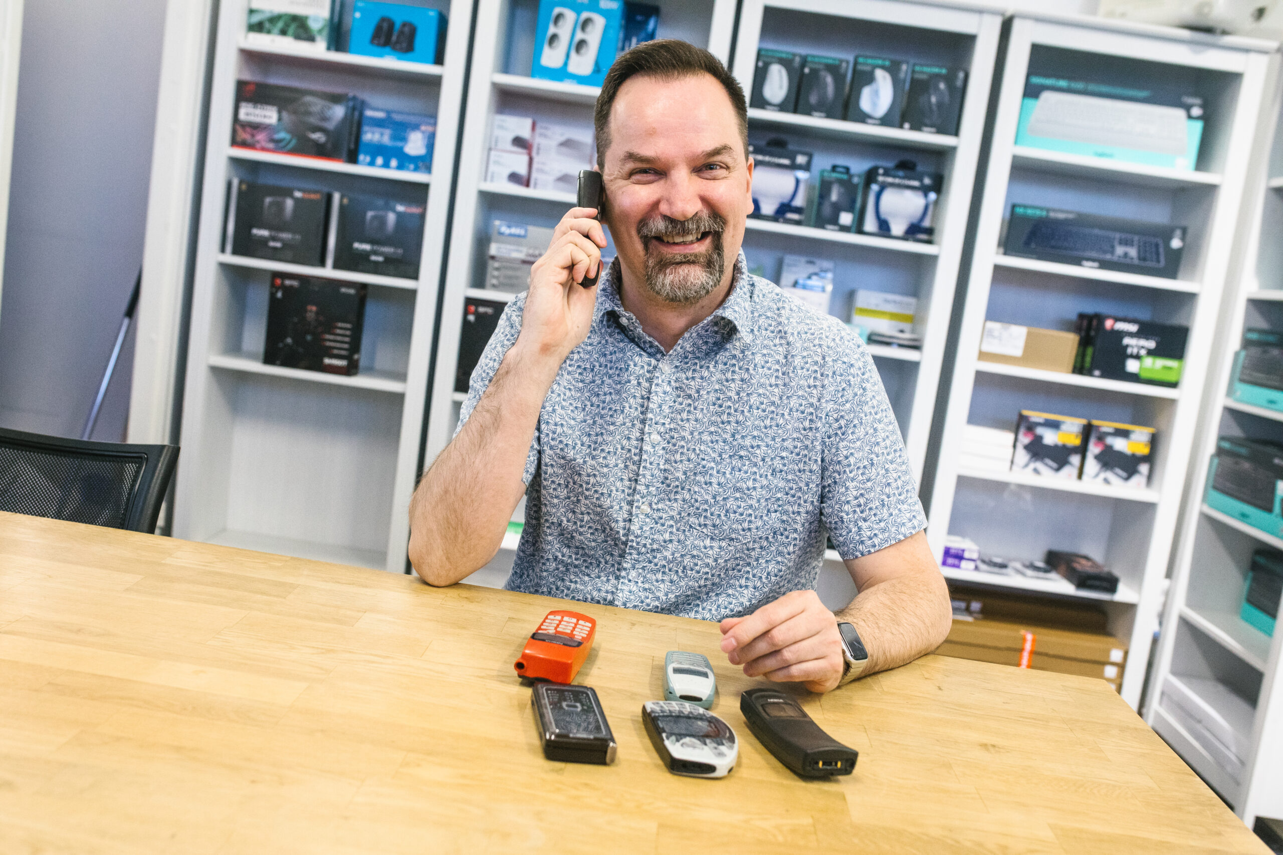 Henkilö puhumassa vanhaan puhelimeen. Edessä vanhoja puhelimia.