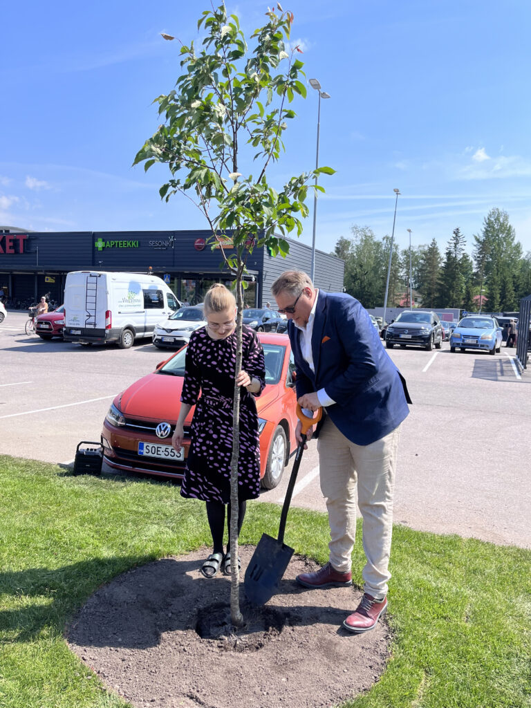 Ihmisiä istuttamassa puuta. Henkilöllä on lapio kädessä.