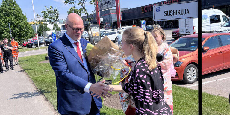 Henkilö ojentaa kukkapuskan puku päällä olevalle henkilölle ja kättelee häntä..