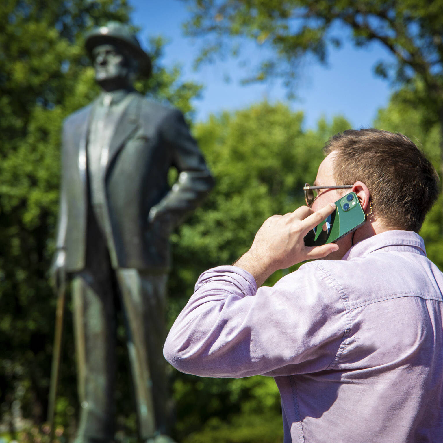 Taustalla Sibelius-patsas, edessä mies puhuu puhelimessa