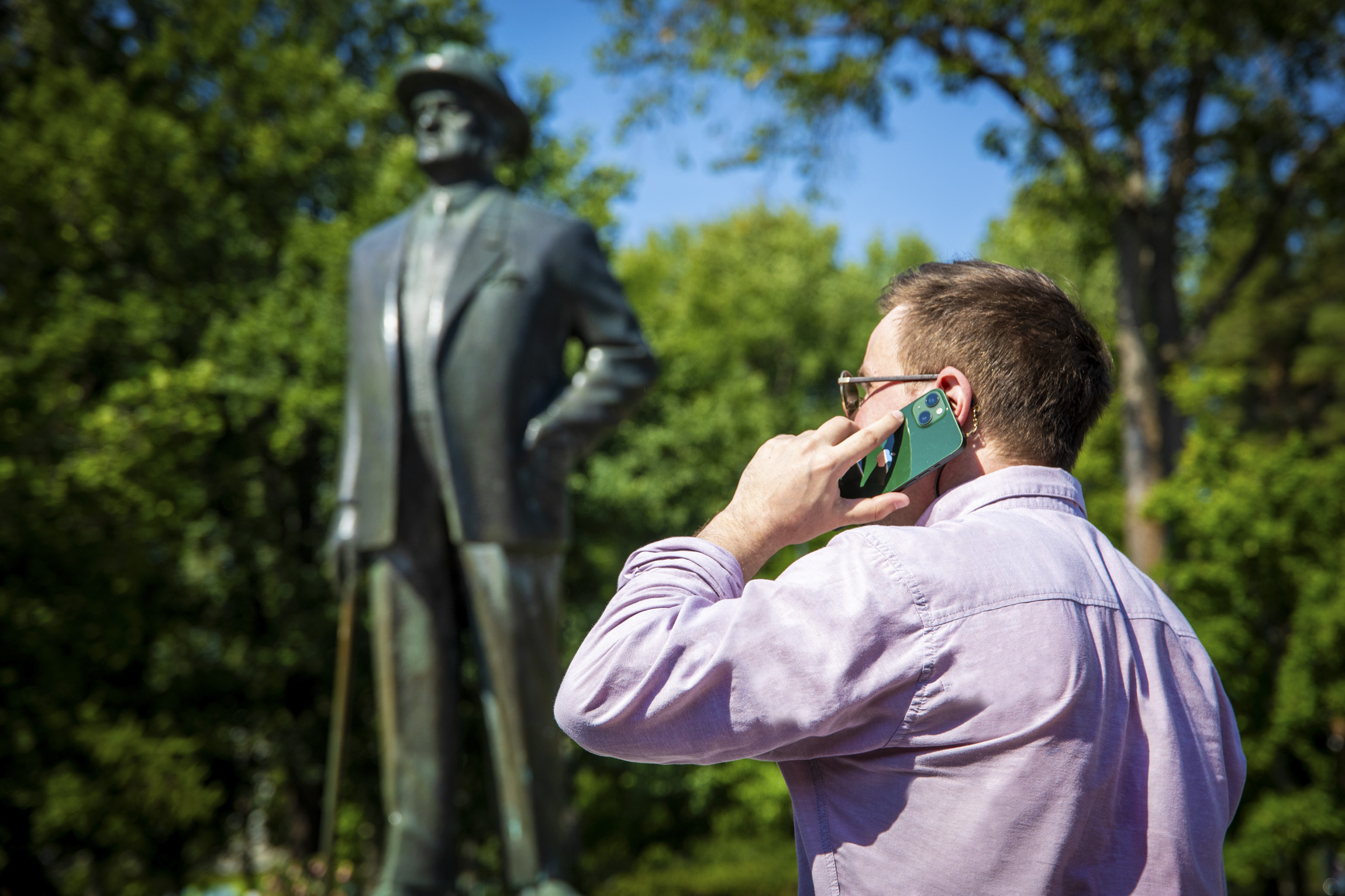 Taustalla Sibelius-patsas, edessä mies puhuu puhelimessa