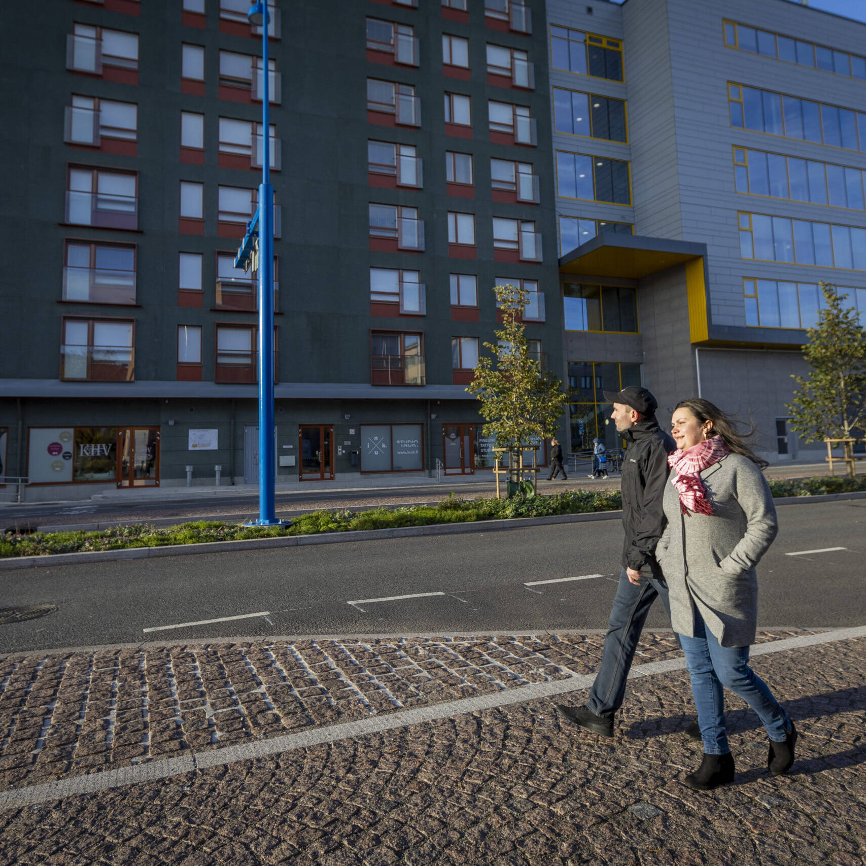 Kaksi henkilöä kävelevät kadulla talon edessä.