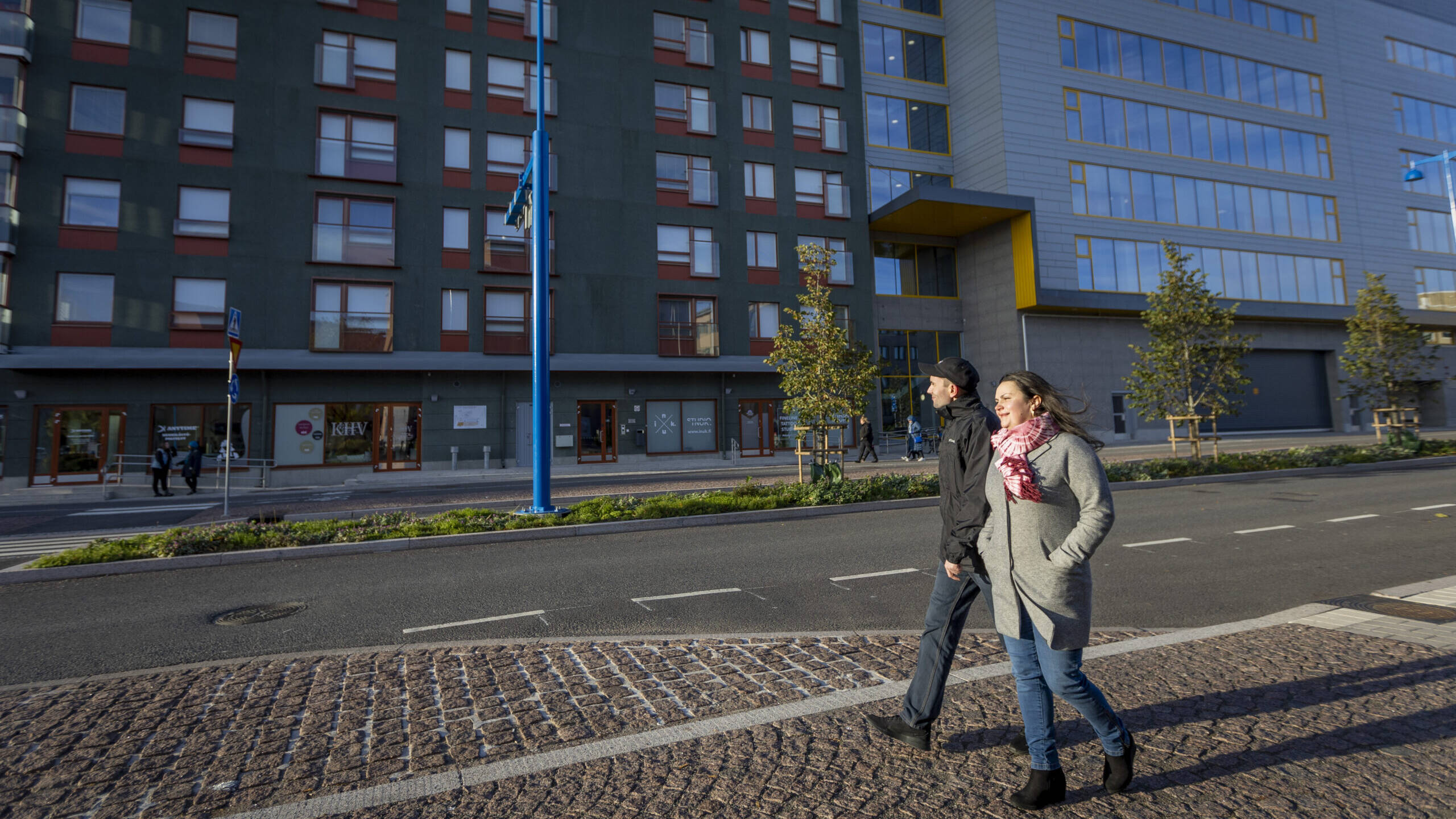 Kaksi henkilöä kävelevät kadulla talon edessä.