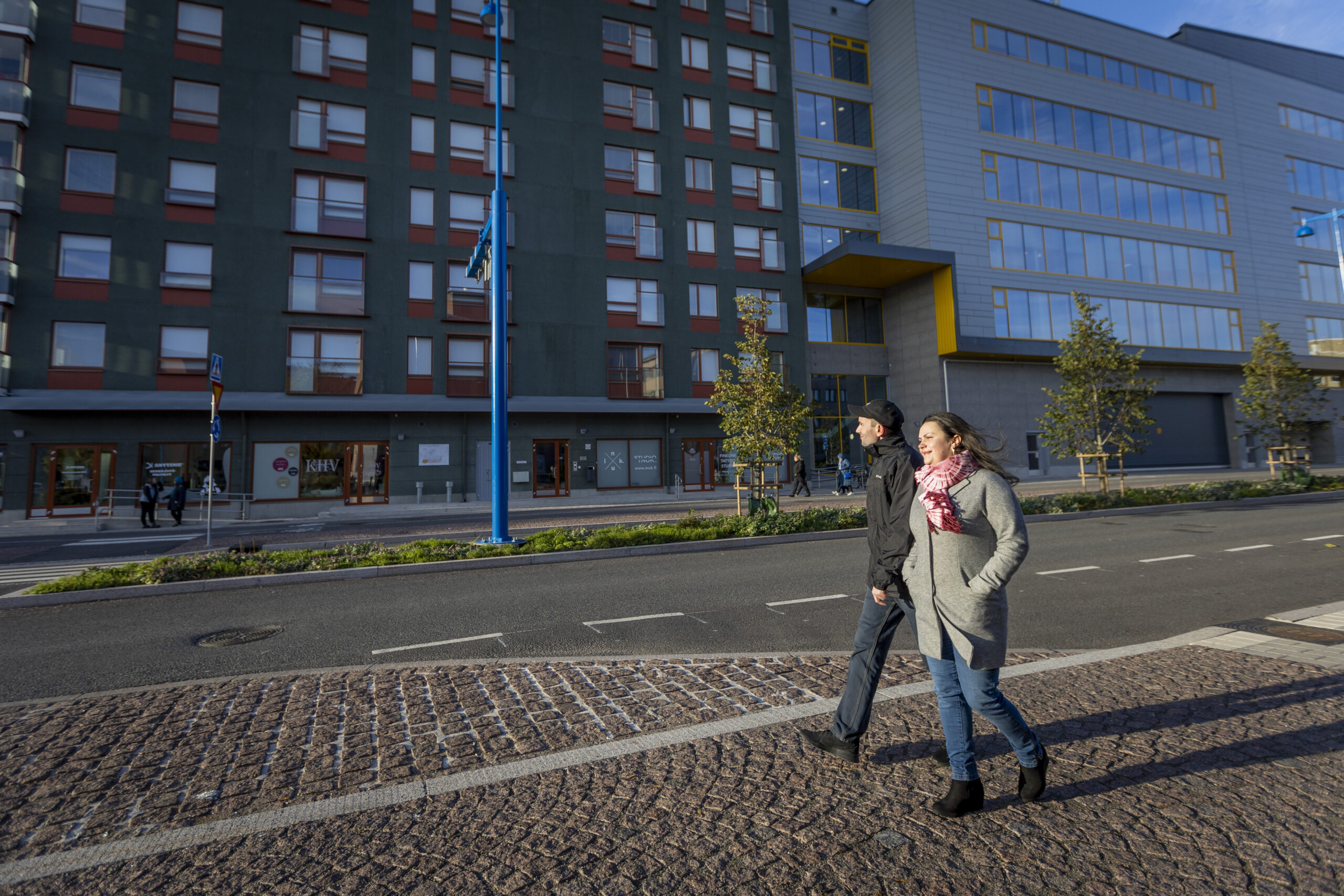 Kaksi henkilöä kävelevät kadulla talon edessä.