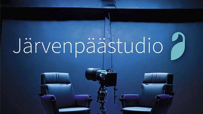 Järvenpäästudion logo tummansinisellä taustalla. Kuvassa kaksi mustaa studiotuolia ja keskellä kamera jalustalla valaistussa studiossa.