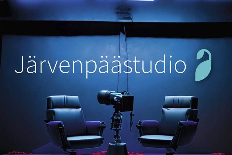 Järvenpäästudion logo tummansinisellä taustalla. Kuvassa kaksi mustaa studiotuolia ja keskellä kamera jalustalla valaistussa studiossa.
