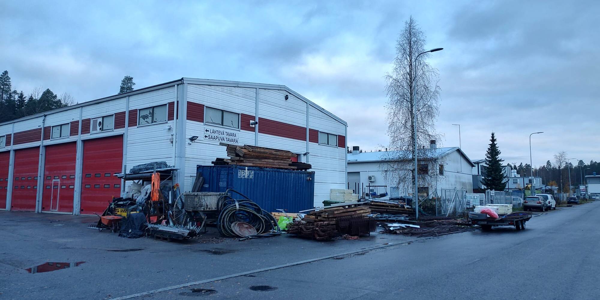 Teollisuusrakennus, jonka edustalla on ajoneuvoja ja työvälineitä.