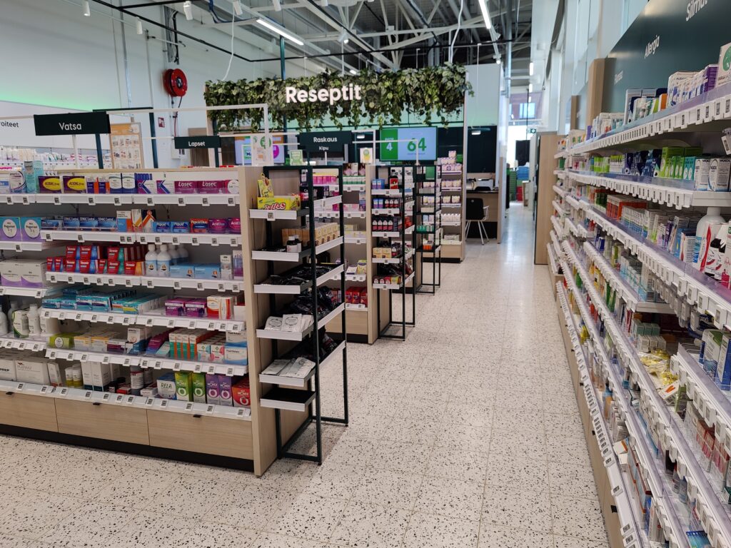 Järvenpään Lähiapteekin valoisa myymälä, jossa hyllyillä on erilaisia apteekkituotteita. Taustalla näkyy viherkasveilla koristeltu reseptipalvelupiste.